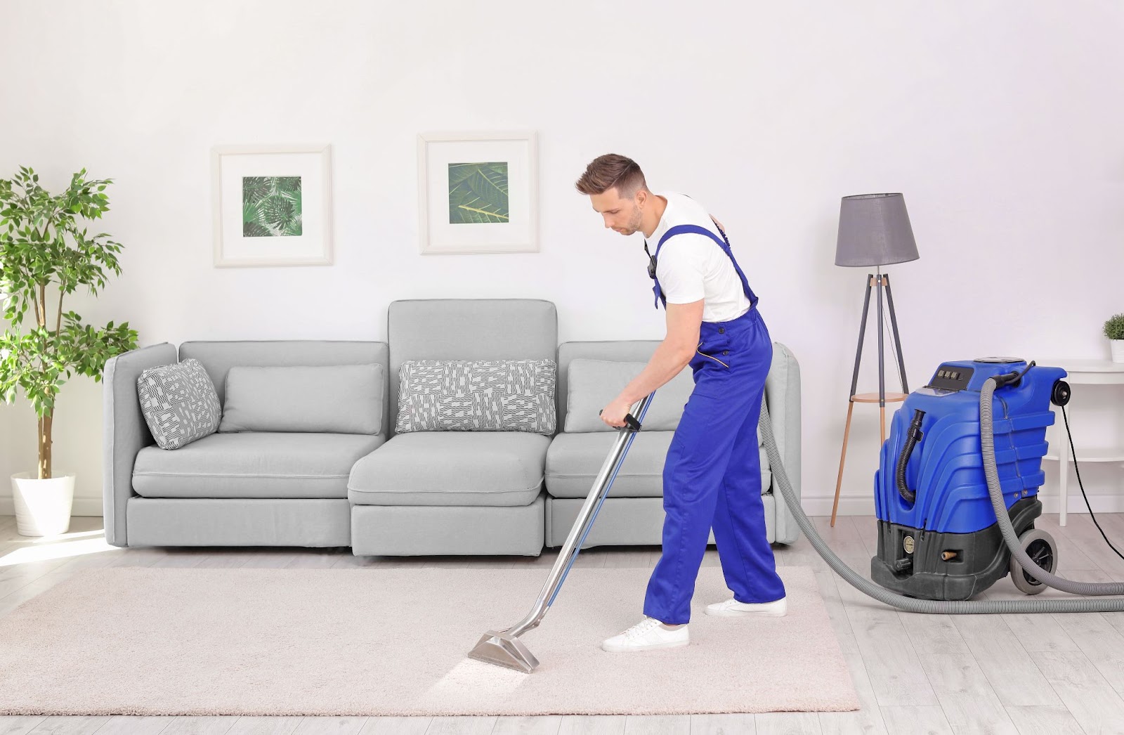 A man in blue overalls using a heavy-duty vacuum to professionally clean a carpet.