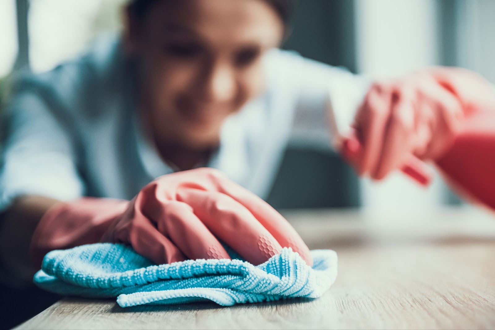 A close-up image of a young woman wearing pink gloves deep cleaning a wooden table.