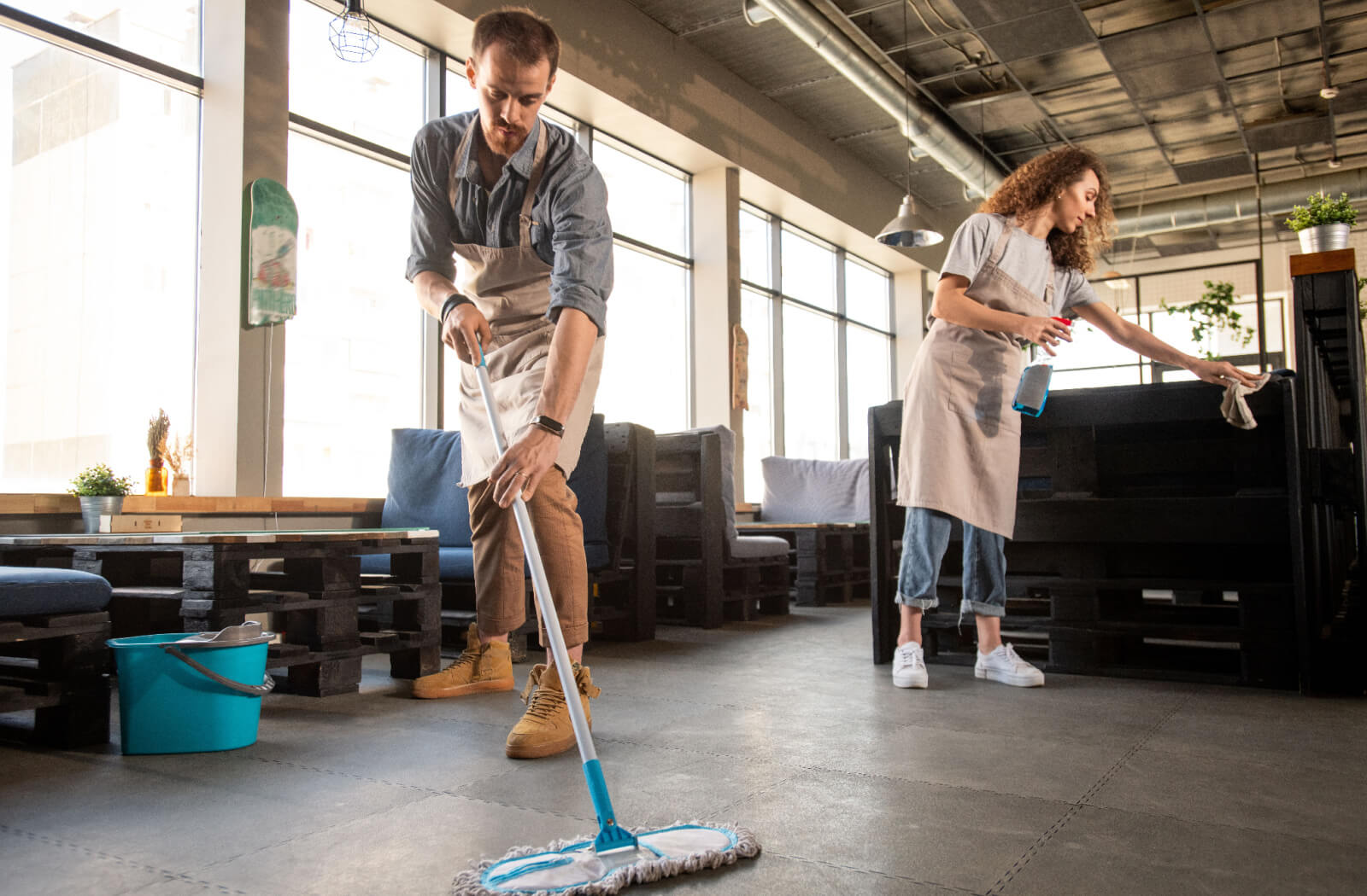 A pair of professional cleaners sweeping and cleaning their restaurant floor and tables to prevent slips and falls.