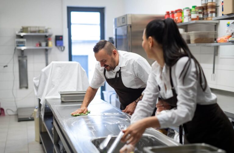 Two staff cleaning a commercial kitchen.