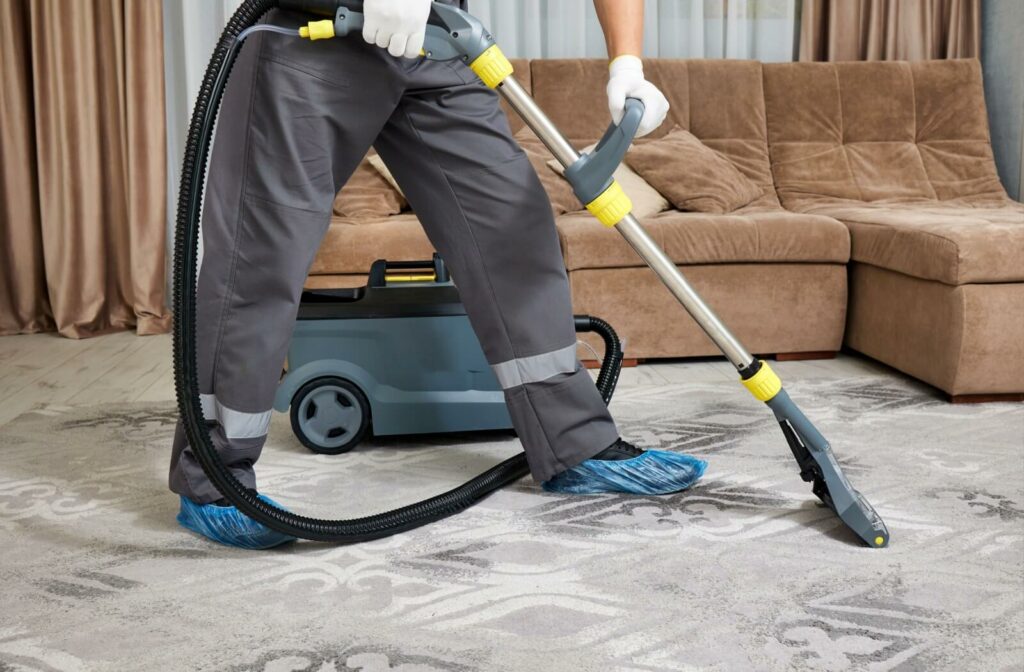 A professional cleaner sports blue shoe covers while wet vacuuming a rug.