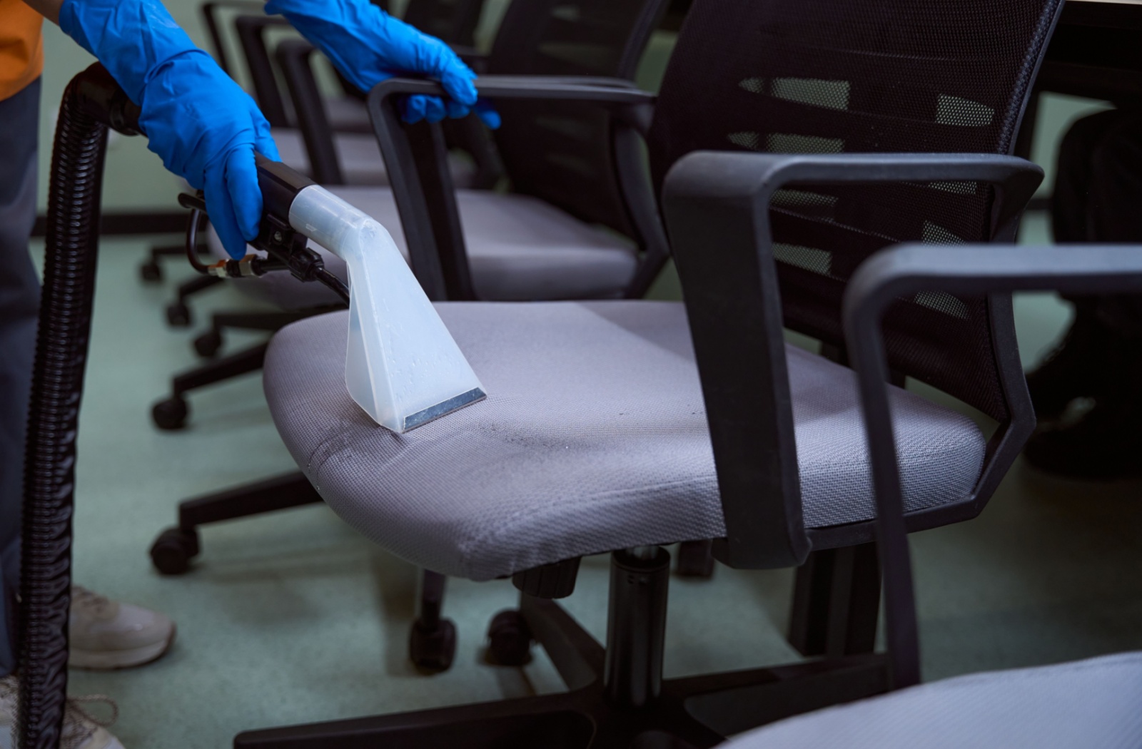 An image of a professional cleaner using a machine to deep clean the seats of many office chairs.