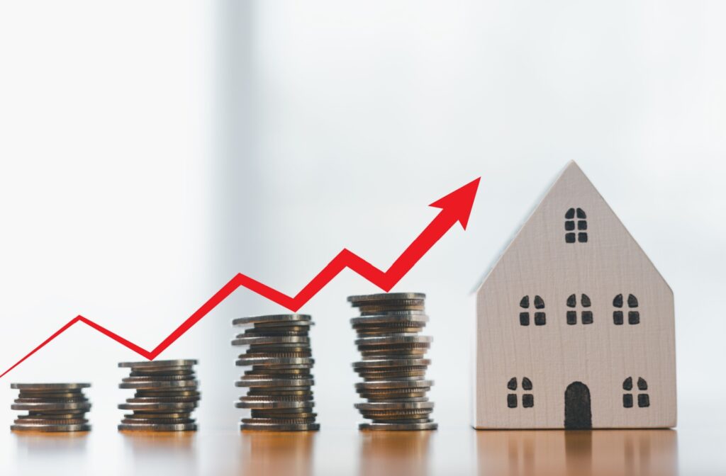 An image of coins stacked in rows that are progressively higher than the previous row, with a house at the end to signify increased home value.