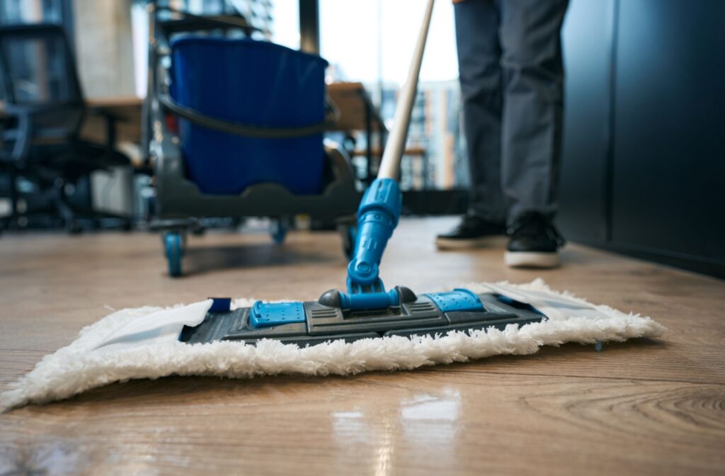 Close-up of a cleaner using a mop to clean shiny hardwood floors.