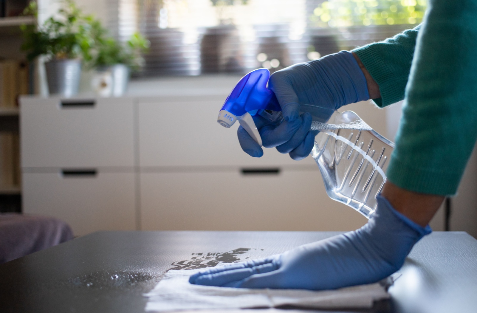 A person wearing gloves using disinfecting spray to clean their table.