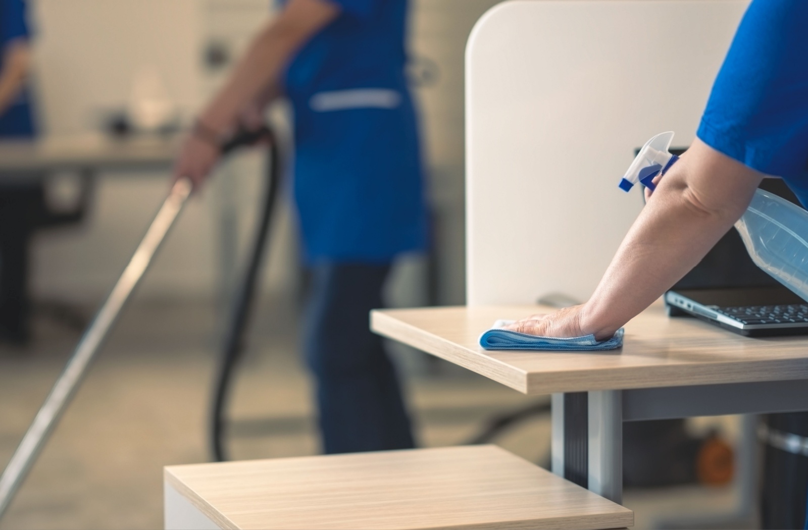 A cleaning team wipes down the desks in an office space.