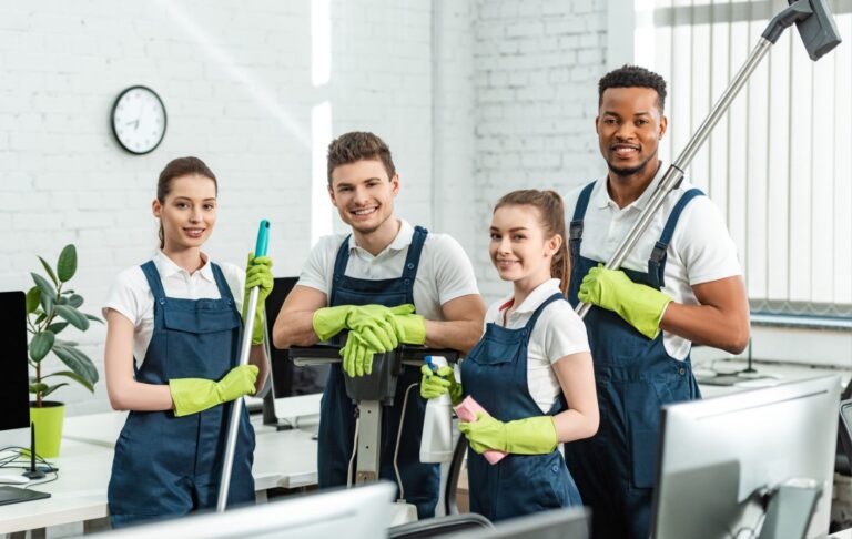 A professional cleaning crew wearing aprons and green gloves pause from cleaning to look up and smile.
