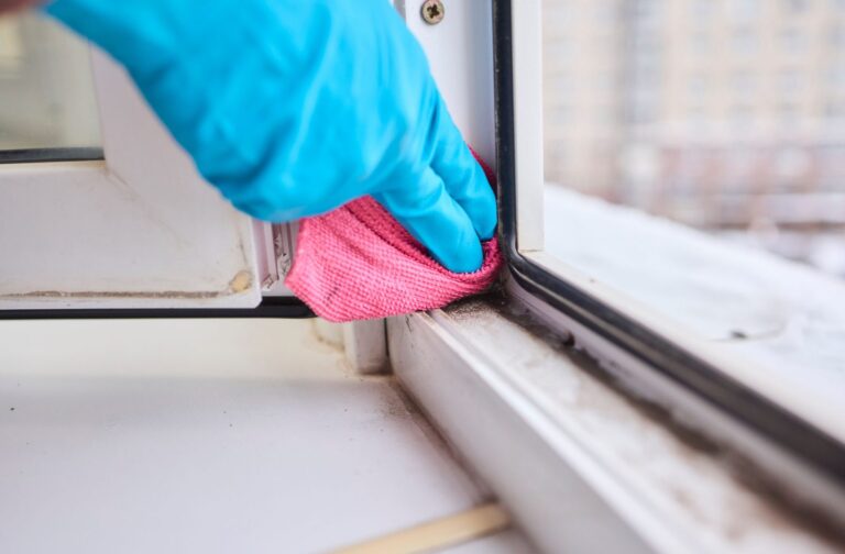 Hand wearing blue glove wiping a window track with microfibre cloth.