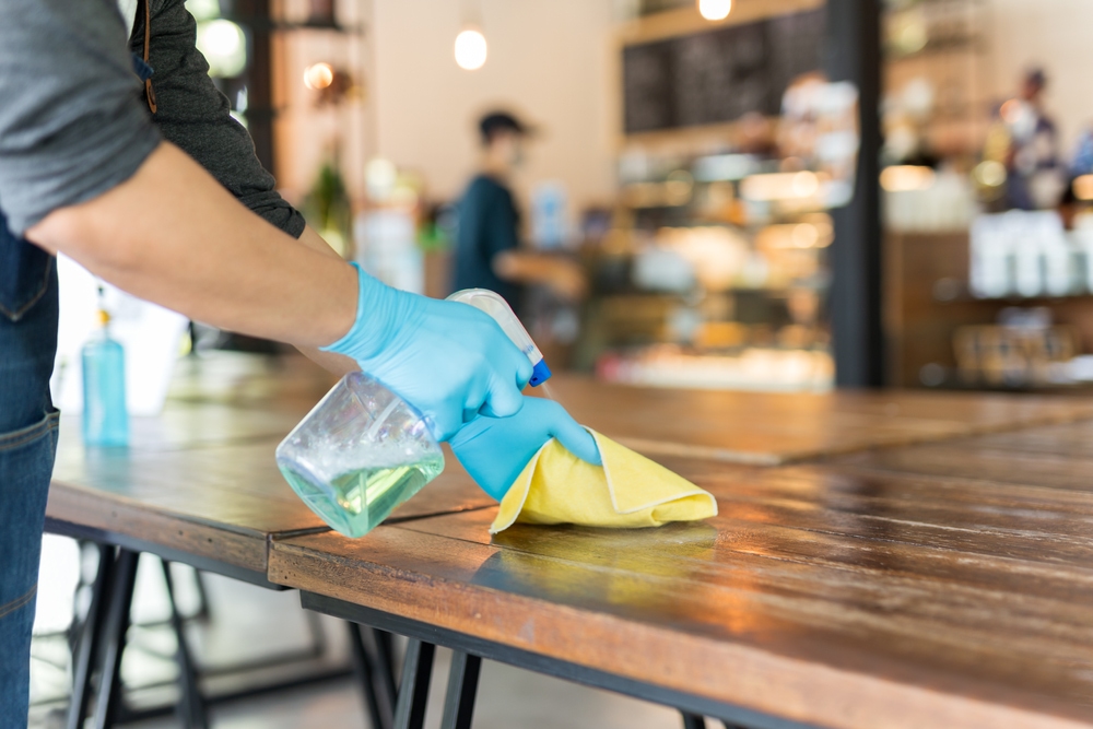 Person spraying and cleaning a tabletop in a restaurant.