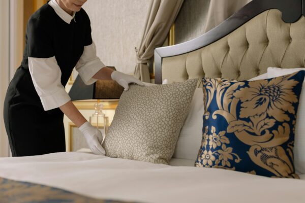Home Cleaning chambermaid arranges pillows in a luxurious hotel room, showcasing comfort and elegance.