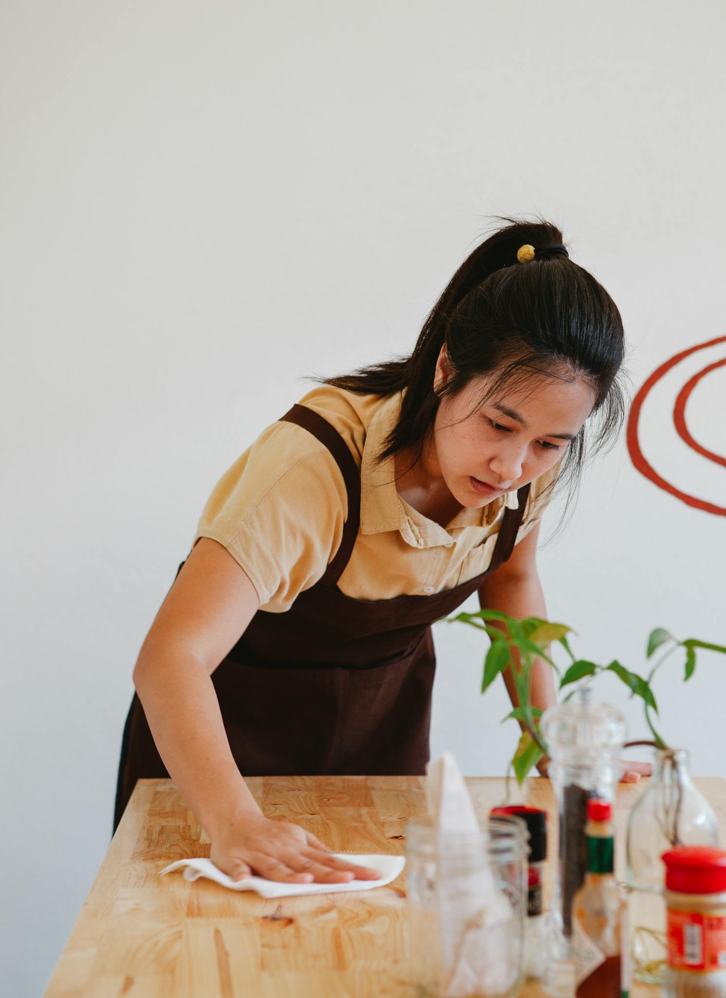 Asian woman wiping a wooden table in a restaurant, showcasing small business operations.
