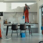 Group of cleaners in red uniforms mopping and wiping glass in a modern dining room.